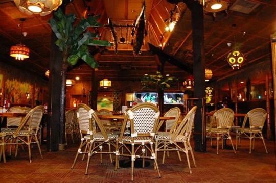 Dining room with rattan chairs, banana-leaf plants and glowing tiki lanterns