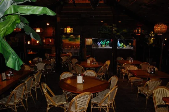 Dimly lit dining room with round wooden tables and a large tropical-fish aquarium