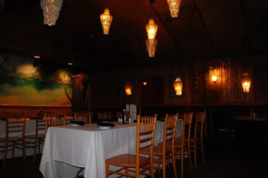 Private dining room with a white-clothed table, crystal chandeliers and a beach mural