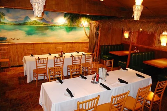 Banquet room set with white-clothed tables in front of a tropical lagoon mural